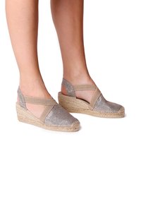 Wedge espadrilles with metallic silver fabric upper, elastic cross-straps, and jute-wrapped heel, highlighting a textured finish.