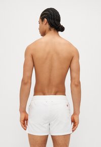 White swim trunks with an elastic waistband, featuring a back pocket and subtle branding. Smooth texture and simple design.
