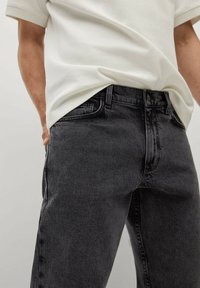 Tummanharmaat suoralahkeiset farkut, joissa on klassinen viiden taskun malli ja hillitty ompelu, yhdistettynä valkoiseen tekstuuripaitaan.