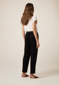 Zwarte taps toelopende broek met een elastische tailleband en zijzakken, gecombineerd met een wit T-shirt met korte mouwen, gezien van achteren.