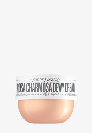 Crème Rosée Charmante Dewy dans un pot rond rose poudré avec un couvercle blanc orné de texte noir et de points décoratifs. Surface lisse, design compact.