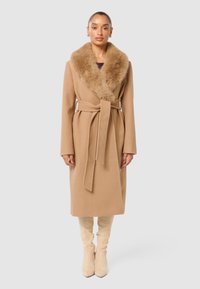 Beige ullrock med en fuskpälskrage, midjebelagd, lång ärm och rak fåll. Matchad med knähöga beige stövlar.