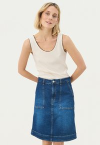 White tank top with black trim and a denim A-line skirt featuring front pockets, a button closure, and a medium blue wash.