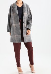 Grå rutig kapp med oversized passform, breda slag och två knappar. I kombination med bordeauxfärgade byxor och beiga högklackade skor.