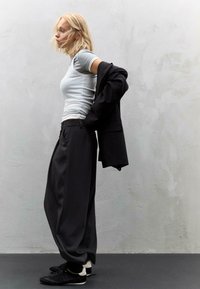 Szara dopasowana koszula, czarne oversize'owe spodnie i czarne buty. Miękkie tekstury, luźne kroje i ciemna paleta barw dominują w tym stroju.