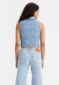 Colete sem mangas de denim azul claro com um design cropped, apresentando costuras nas costas e uma etiqueta na cintura de jeans azuis claros combinando.