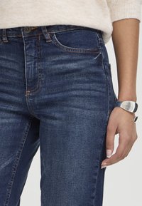 Jeans en denim bleu foncé avec une coupe slim, dotés d'une ceinture classique, de poches avant et d'un léger effet usé. Agrémentés de coutures orange.