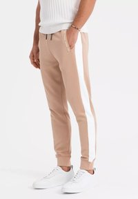 Tan atleet joggers met witte zijstrepen, tapered fit, elastische tailleband, ritszakken en geribde manchetten, gecombineerd met witte sneakers.