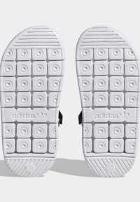 White sandal soles with circular and square traction patterns, featuring the Adidas logo embossed in the center of each sole.