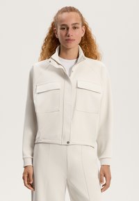 Weißes, kurzes Jackett aus weichem Stoff mit Reißverschluss, hohem Kragen und zwei Brusttaschen mit Klappen. Glatte Textur.