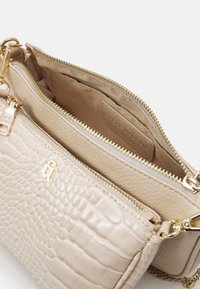 Béžová crossbody taška s krokodýlí texturou, zlatými kovovými doplňky a zipovou přihrádkou. Uvnitř je měkká podšívka a kapsa na karty.