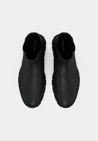 Schwarze Leder-Schlüpfschuhe mit glatter Oberfläche, abgerundeter Zehe und strukturiertem Gummisohle für besseren Halt. Einfaches Design mit minimalen Details.