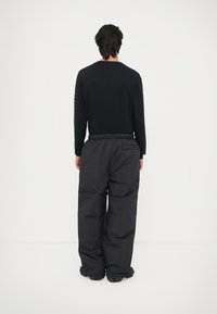 Maglietta nera a maniche lunghe con testo stampato sulla manica, abbinata a pantaloni neri larghi e voluminosi con tasca posteriore e cintura elastica.