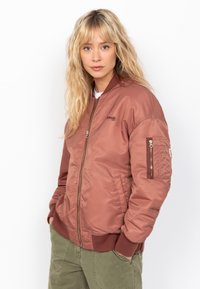 Bomber jacket de acabado satinado en rosa apagado, con cremallera frontal, puños de canalé y un bolsillo en el pecho con detalle de cremallera.