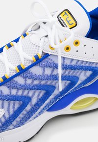Chaussure de sport blanche, bleue et jaune avec empeigne en mesh, lacets blancs et coussin d'air visible dans la semelle près du talon.