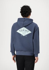 Felpa blu navy in cotone con tasca a marsupio, presenta un grande logo bianco a forma di diamante sul retro con testo e anno di fondazione.