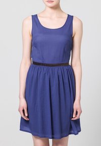 Lila mekko ilman hihoja, jossa on vartalonmyötäinen yläosa, kerroksellinen hame ja teksturoitu ruskea vyö vyötäröllä. Tasainen kangas, jossa on kevyt kiilto.