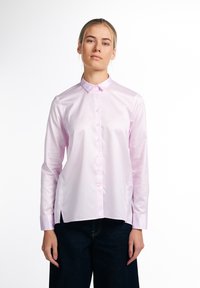 Helles rosa, langärmliges Hemd mit Knopfleiste aus glattem Stoff; verfügt über einen klassischen Kragen und seitliche Schlitze. Kombiniert mit dunklen Jeans.