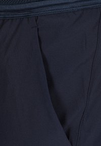 Gros plan sur un tissu noir avec une couture visible et des détails de surpiqûres à la ceinture, présentant une texture lisse et des plis subtils.