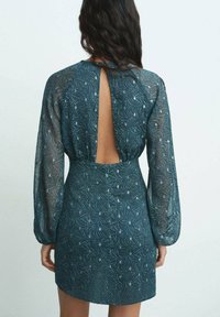 Teal kort klänning med en texturerad mönster, långa genomskinliga ärmar och en djup utskärning i ryggen. Figursydd midja med en utsvängd kjol.