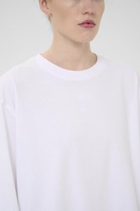 Tricou alb din bumbac, cu guler rotund, croială lejeră și logo brodat pe piept. Textură netedă și mâneci scurte.