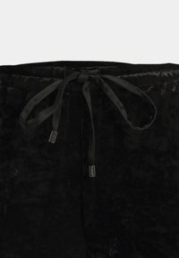 Pantalon en velours noir avec une taille à cordon de serrage, présentant une texture lisse et un éclat subtil. Comprend des accents de quincaillerie de marque.