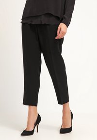 Svarta tapered byxor med en slät textur, med hög midja och kort längd, ihopparade med spetsiga svarta stilettklackar.