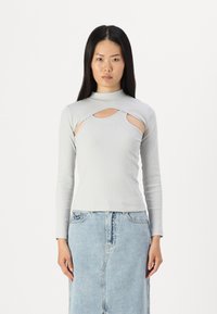 Top lung cu maneci lungi, de culoare gri deschis, cu guler înalt și detalii decupate pe laterale. Combinat cu o fustă din denim albastru.