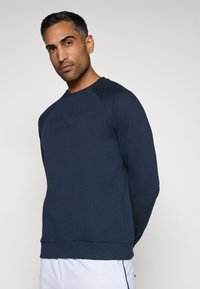 Felpa navy realizzata in tessuto morbido, con collo a giro e maniche lunghe, e testo in rilievo sul petto. Polsini e orlo a costine.