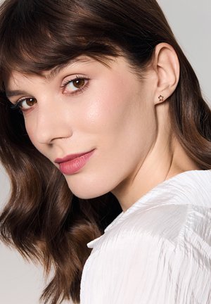 Złote kolczyki w kształcie gwiazd; modelka z brązowymi włosami, nosząca białą, strukturalną bluzkę; gładka skóra, naturalny makijaż i neutralny kolor ust.