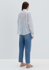 Camicia button-up blu chiaro realizzata in un tessuto morbido e fluido; presenta una vestibilità comoda, maniche lunghe e un orlo curvo. Abbinata a jeans blu scoloriti.