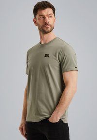 Olive green short-sleeve t-shirt made of cotton, featuring a round neckline and a small black label on the chest. Smooth texture.
