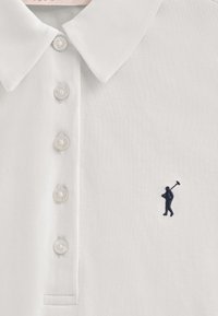 Biała koszulka polo z teksturowanej tkaniny z kołnierzykiem zapinanym na guziki. Posiada pięć guzików oraz granatową haftowaną strukturę golfa na piersi.