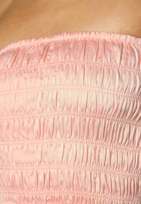 Vestido sem alças em cetim rosa suave, com textura franzida e detalhes de costura horizontal, criando uma silhueta ajustada.