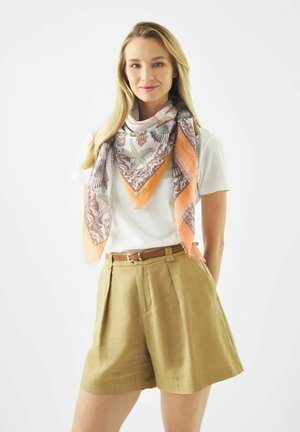 Frau trägt beige High-Waist-Shorts, weißes kurzärmeliges Hemd, braunen Gürtel und einen großen orangefarbenen, gemusterten Schal um den Hals.