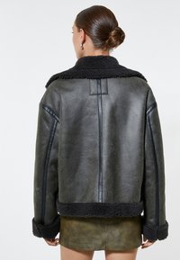 Zwarte shearling-gevoerde, faux leren jas met een brede kraag, een effen groene body en nauwsluitende mouwen. Beschikt over een gestructureerd oppervlak en gestikte details.