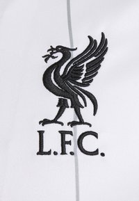 Oiseau Liver noir brodé tenant une branche au-dessus de "L.F.C." sur fond de tissu blanc.