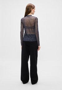 Top lungo a strisce nero e blu trasparente con una silhouette aderente, abbinato a pantaloni neri comodi. Design minimalista.