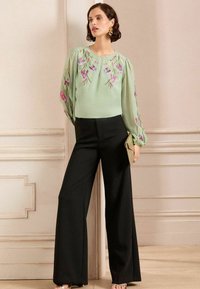 Zaļš blūze ar ziedu izšuvumiem, apvienota ar melnām platām biksēm. Plūstošs audums un balonu piedurknes, papildinātas ar zelta somu.