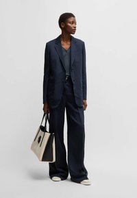 Navy suit featuring a tailored blazer and loose trousers, paired with a black and cream tote bag, and light-colored shoes.