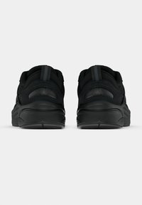 Czarne buty sportowe z teksturowanym wierzchem, wyściełanym kołnierzem i wyraźnym designem pięty. Gładka podeszwa z lekkim zakrzywieniem dla stabilności.