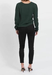 Ciemnozielony sweter z prążkowanej tkaniny z długimi rękawami, zestawiony z czarnymi dopasowanymi spodniami i czarnymi szpilkami, widok z tyłu.