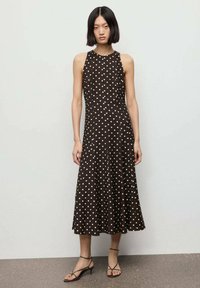 Vestido marrón sin mangas con lunares blancos, con dobladillo acampanado y tejido ligero. Combinado con sandalias negras de tiras.