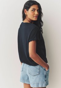 Mustmust triikiga must t-särk, millel on lainelised ääred, koos helesiniste denimsärgiga, millel on esipockets ja vabalt langev lõige.