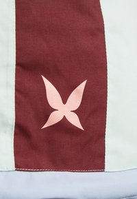 Czerwony i jasnoniebieski materiał o gładkiej fakturze, z różowym logo motyla na czerwonej części. Wyraźne detale szwów.