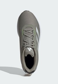 Scarpa atletica grigia con tomaia in rete perforata, lacci rotondi e accenti verdi. Presenta una suola imbottita e dettagli testurizzati.
