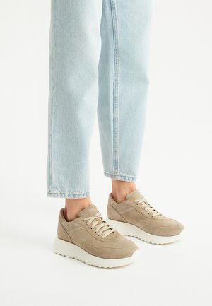Sneaker in suede beige con suola bianca spessa, dotate di lacci chiari e dettagli cuciti, abbinate a jeans in denim blu chiaro a gamba dritta.