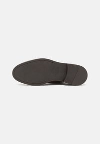 Suola di scarpa in pelle marrone scuro con superficie testurizzata, forma arrotondata e dettagli minimi. Presenta cuciture lungo il bordo e marchi del brand.