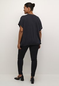 Top nero a maniche corte, dalla vestibilità comoda, con tessuto strutturato e orlo elastico. Abbinato a jeans skinny neri e scarpe con tacco nere.