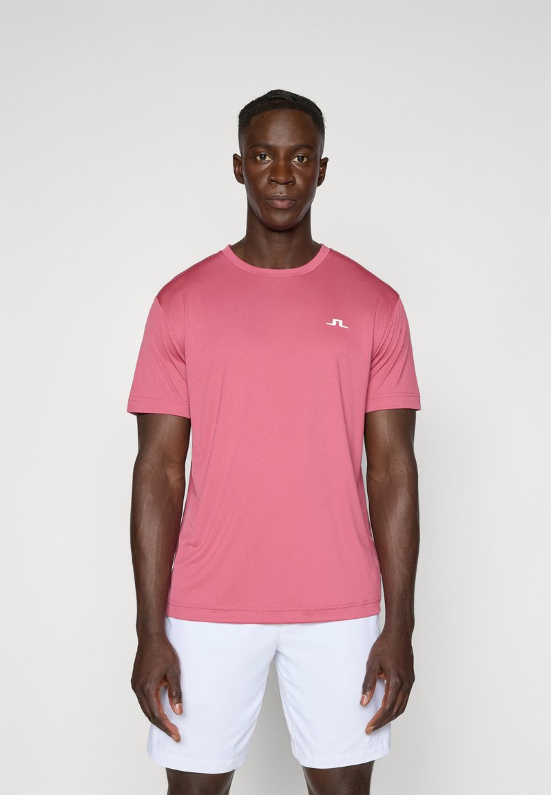 Gaiša rozā īsām piedurknēm, apaļā izgriezuma T-krekls, izgatavots no elpojoša auduma, ar mazu baltu logotipu uz kreisā krūšu daļas.